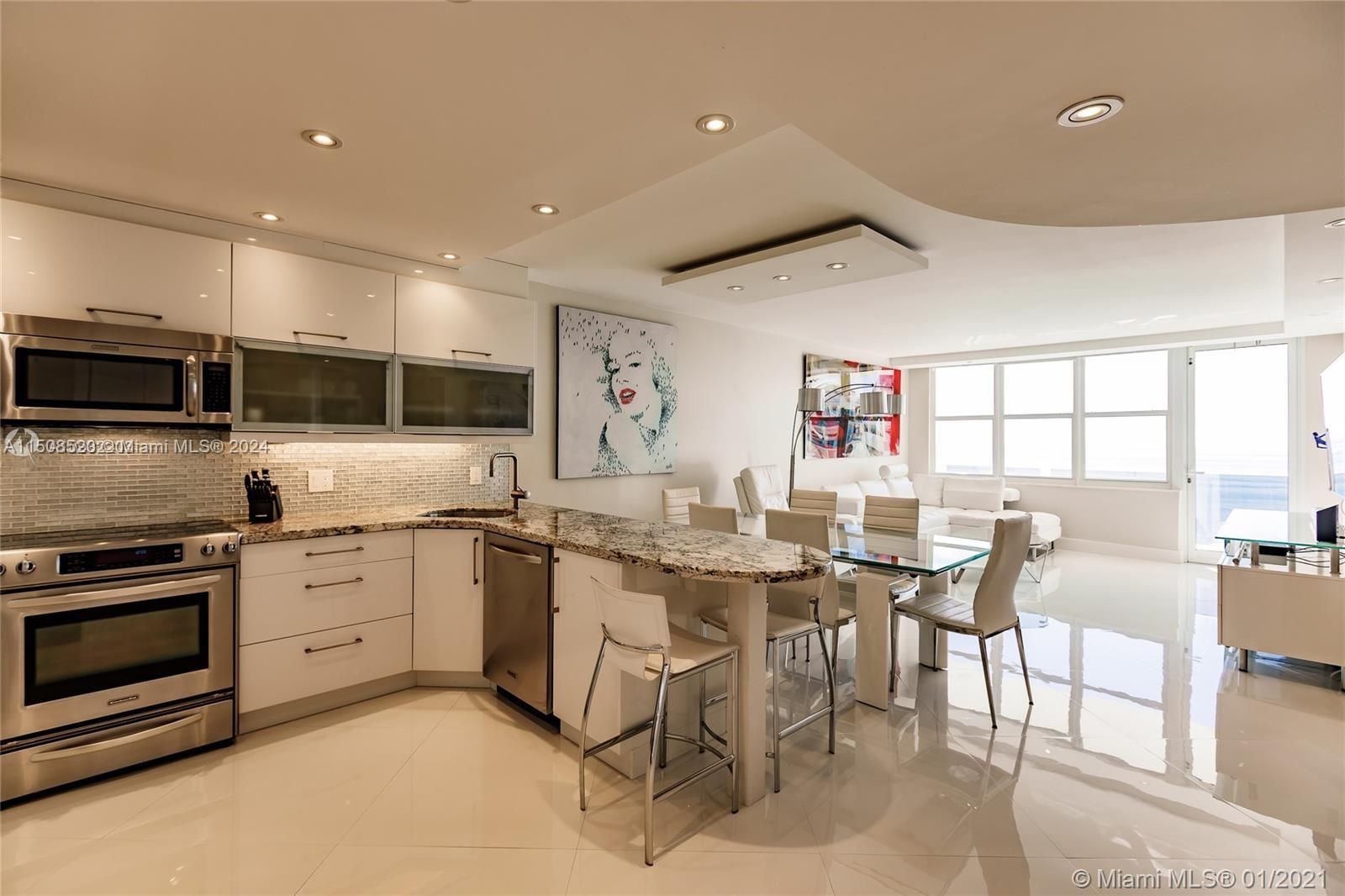 A modern kitchen features white cabinets, granite countertops, and a dining area with white chairs — 3725 S Ocean Dr # 1504, Hollywood FL 33019, HOLLYWOOD, FL