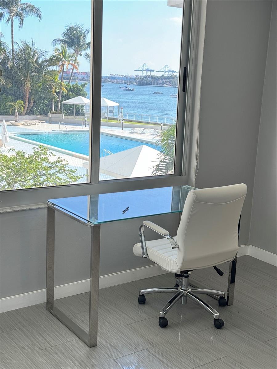 A glass desk and white office chair sit before a window overlooking a pool and harbor — 1200 West Ave # 202, Miami Beach FL 33139, MIAMI BEACH, FL