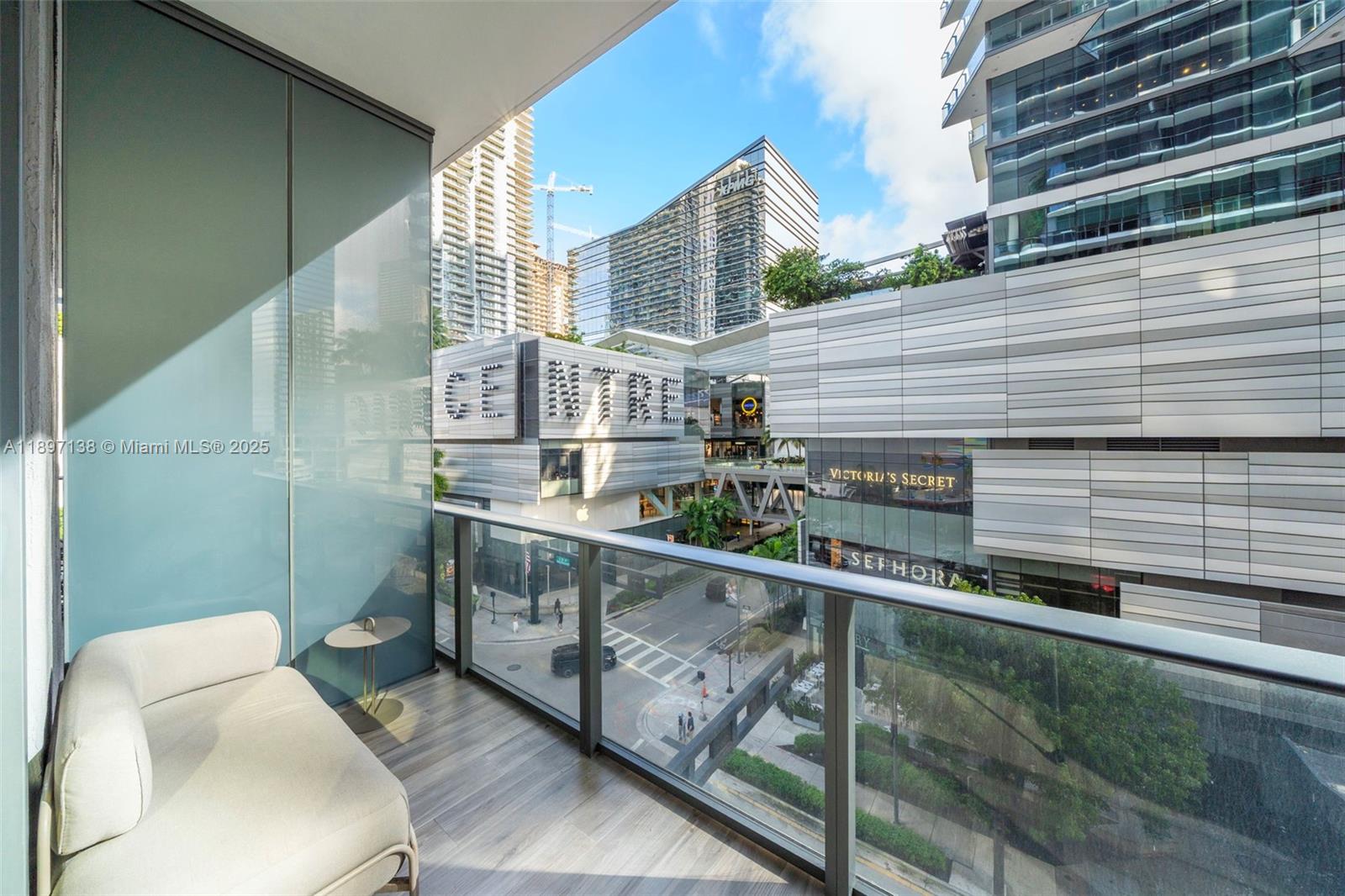 A balcony with a sofa overlooks a city street and modern commercial buildings — 801 S Miami Ave # 402, Miami FL 33130, MIAMI, FL