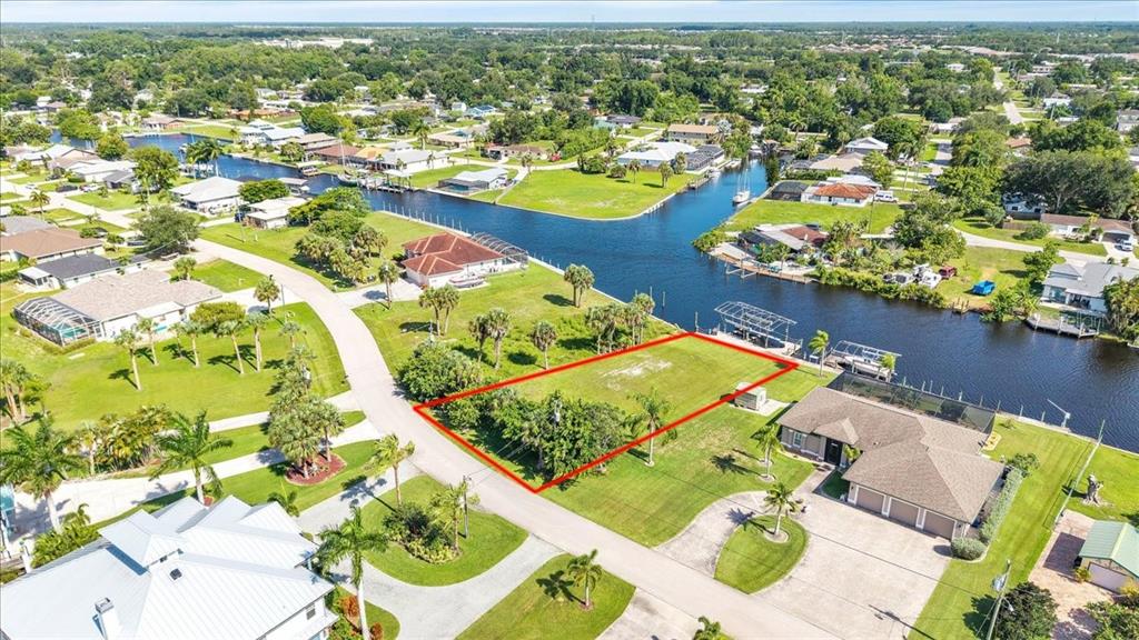An aerial view shows a vacant waterfront lot outlined in red within a residential neighborhood — 13425 MARQUETTE BOULEVARD, FORT MYERS, FL