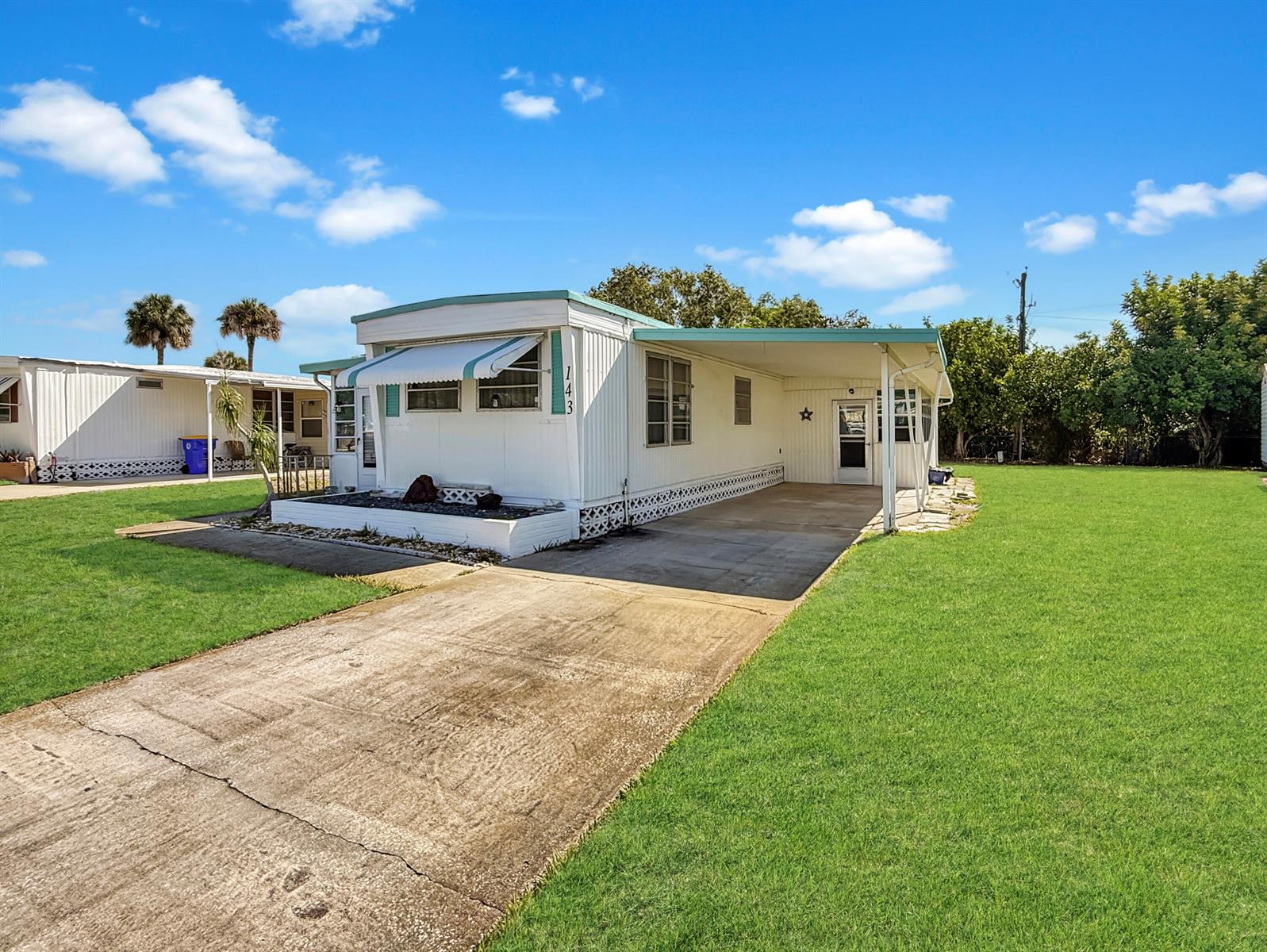 A white mobile home features a concrete driveway, a carport, and a small front garden — 143 SE Easy Street, Stuart FL 34994, STUART, FL