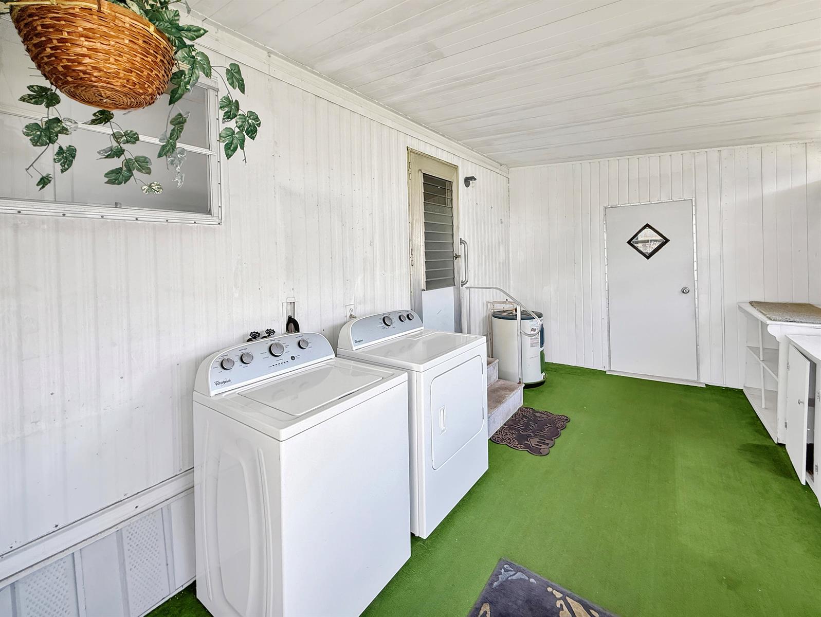 A laundry room features white paneled walls, green carpeting, and a washer and dryer set — 143 SE Easy Street, Stuart FL 34994, STUART, FL