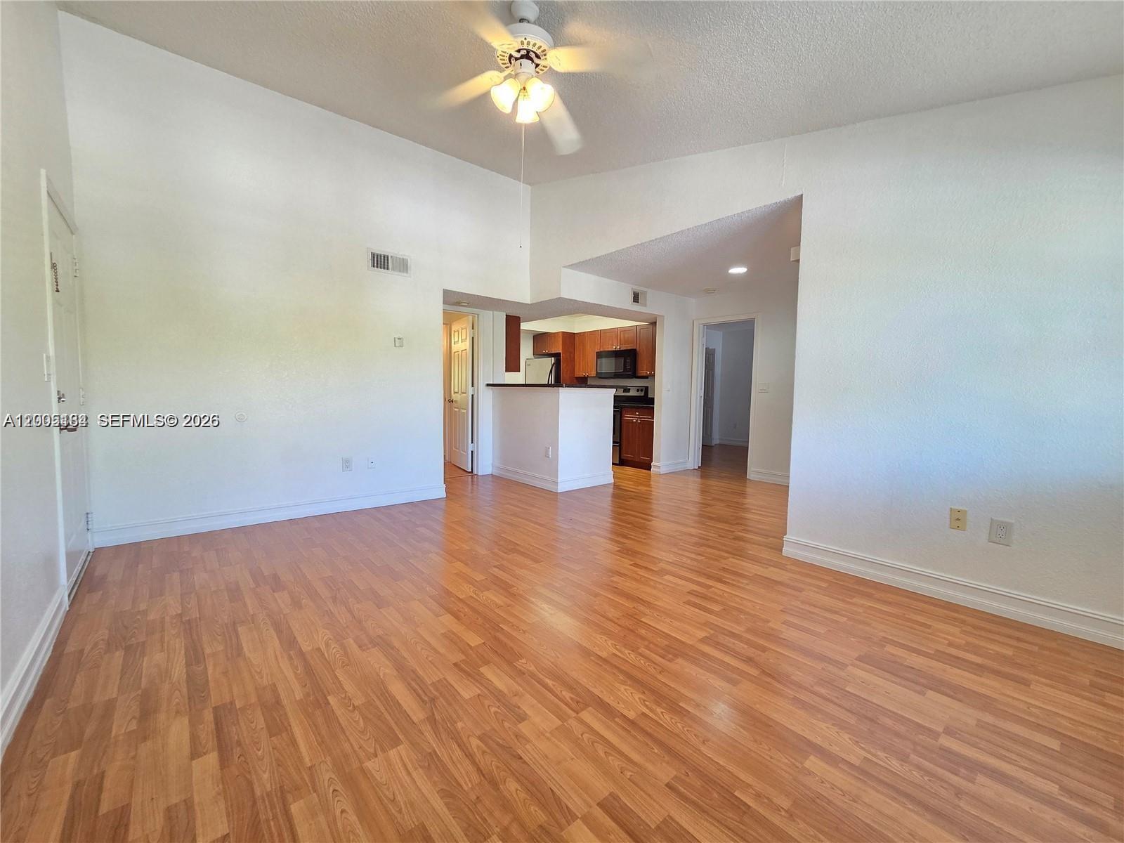 An empty living room with wood-look flooring, a ceiling fan, and an adjacent kitchen — 15650 SW 105th Ln # 502, Miami FL 33196, MIAMI, FL