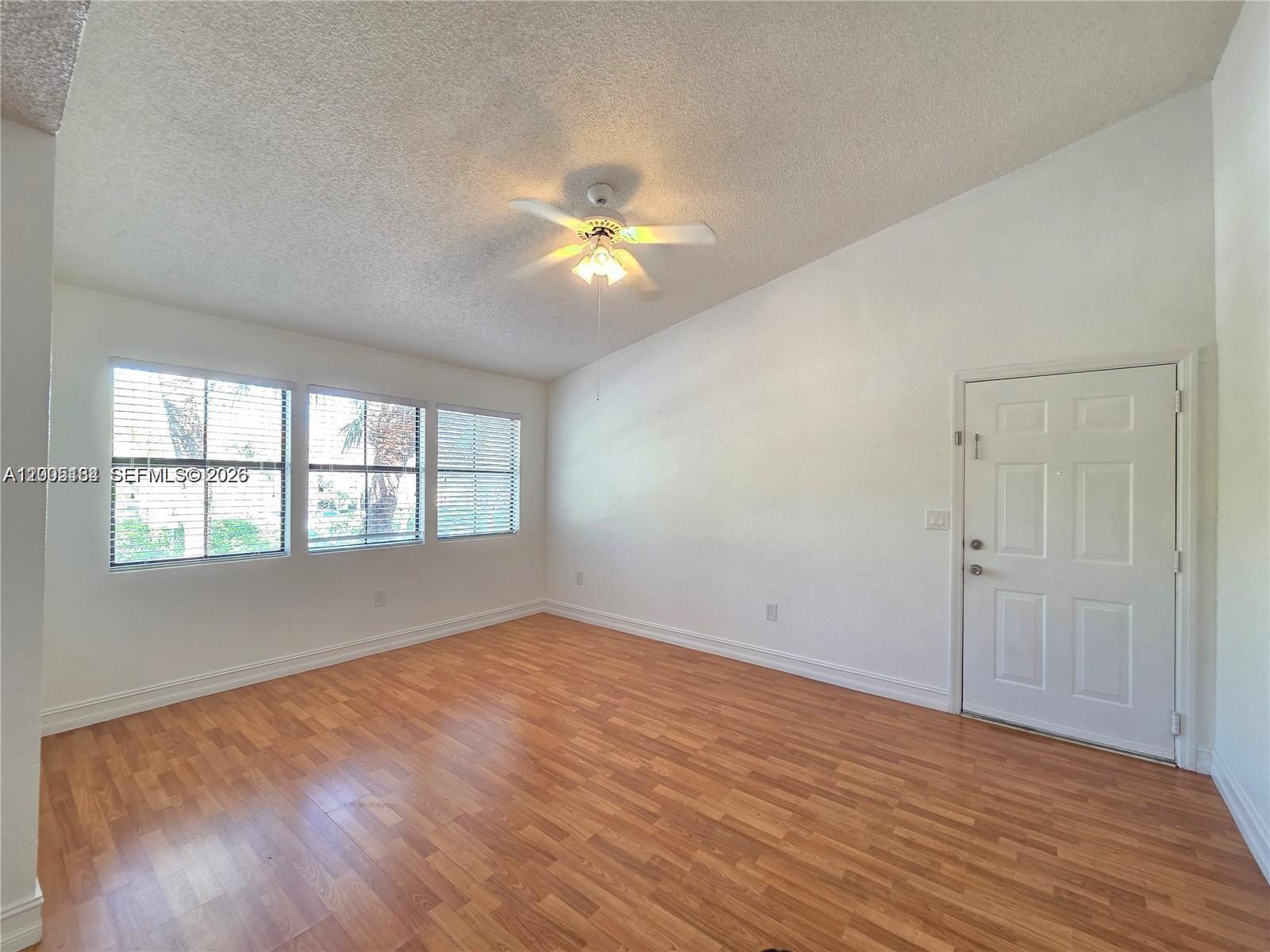 An empty room features wood-look flooring, white walls, a ceiling fan, and three windows — 15650 SW 105th Ln # 502, Miami FL 33196, MIAMI, FL