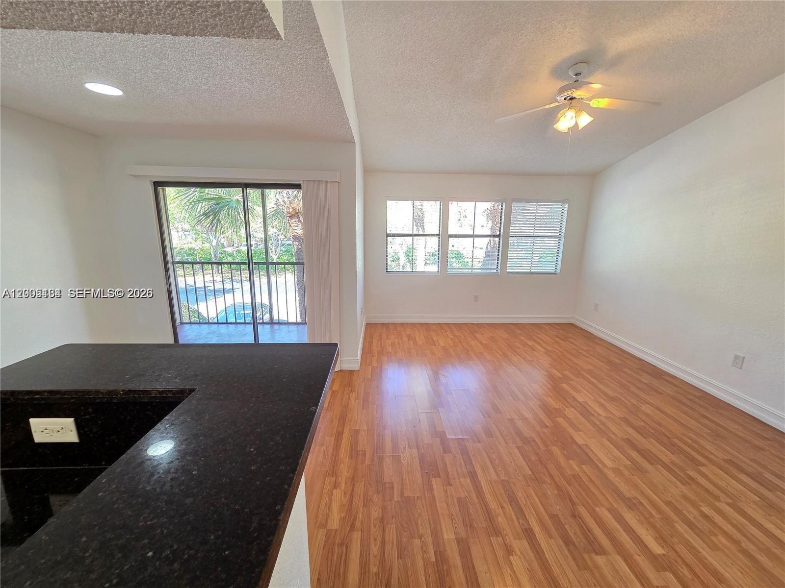 An open living area features wood-look flooring, a ceiling fan, and a sliding glass door — 15650 SW 105th Ln # 502, Miami FL 33196, MIAMI, FL