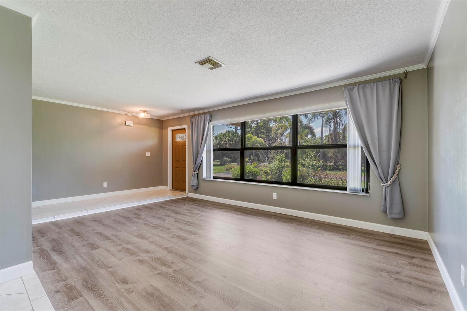 An empty living room features wood-look flooring, gray walls, and a large window with curtains — 7107 181st Street N, Jupiter FL 33458, JUPITER, FL