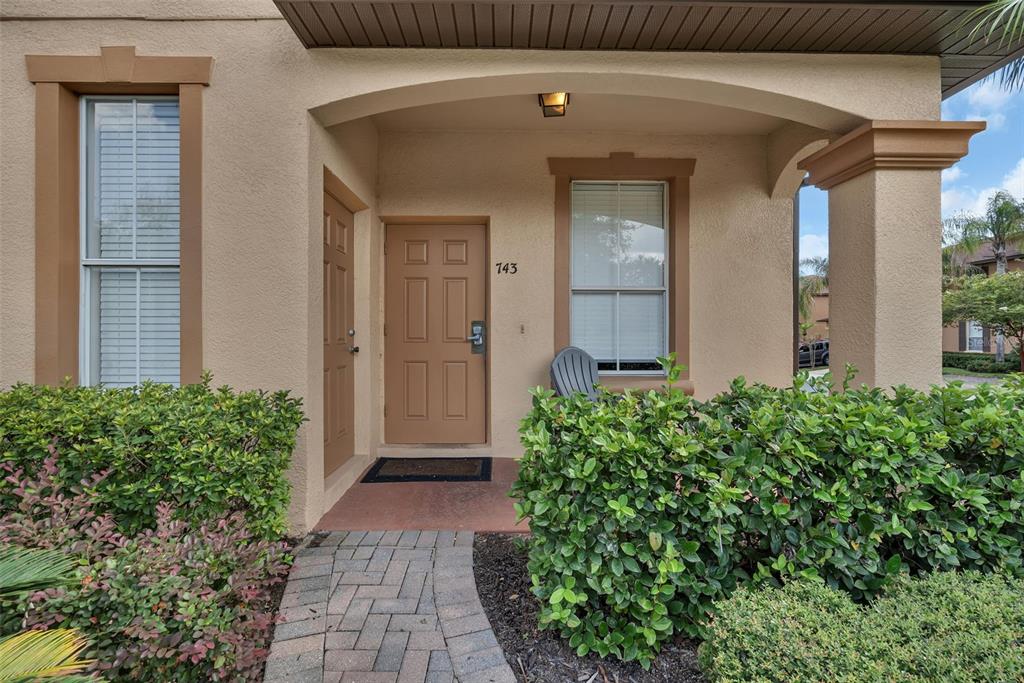 A beige stucco building exterior features a front door, a walkway, and surrounding green bushes — 743 CALABRIA AVENUE, DAVENPORT, FL