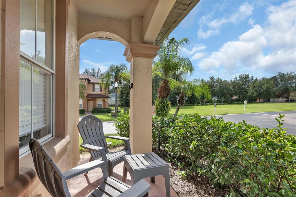 A covered porch features two gray chairs and a small table overlooking a grassy area — 743 CALABRIA AVENUE, DAVENPORT, FL