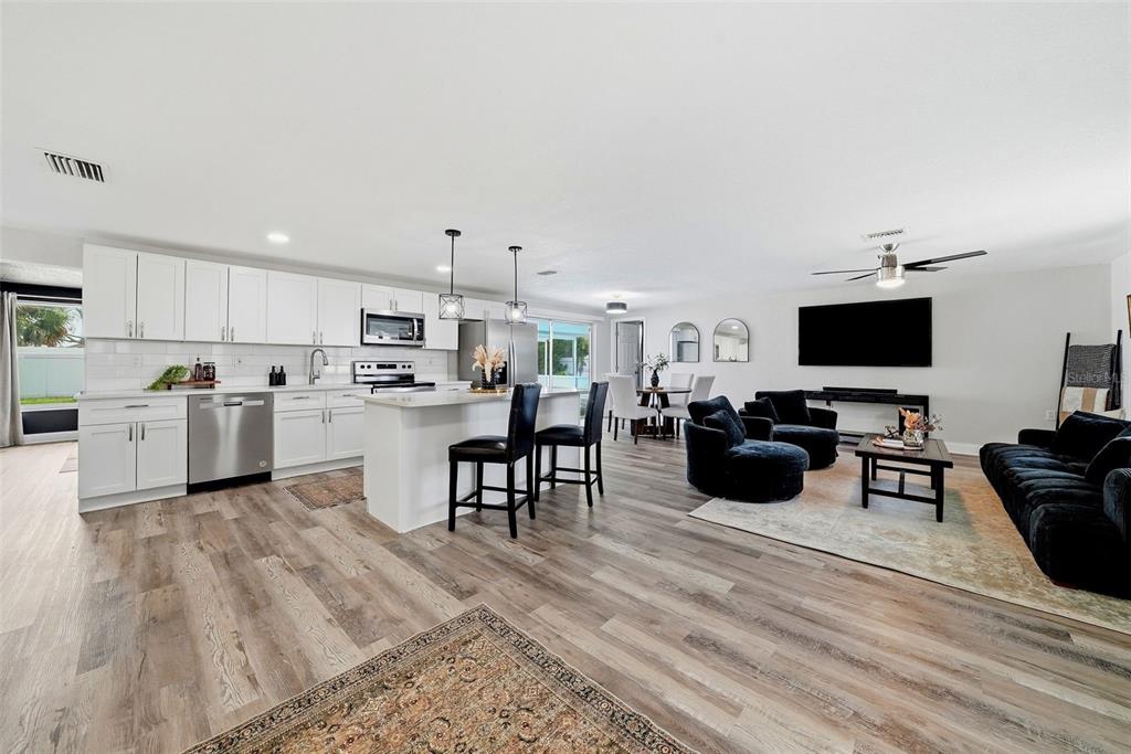 An open-concept kitchen and living area with white cabinetry, stainless appliances, and wood-look flooring — 6072 AIRMONT DRIVE, SPRING HILL, FL