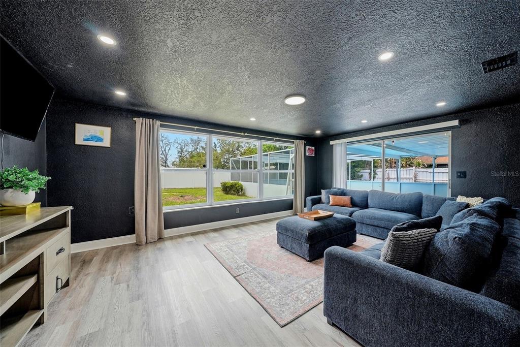 A living room features dark walls, a blue sectional sofa, and light wood-look flooring — 6072 AIRMONT DRIVE, SPRING HILL, FL