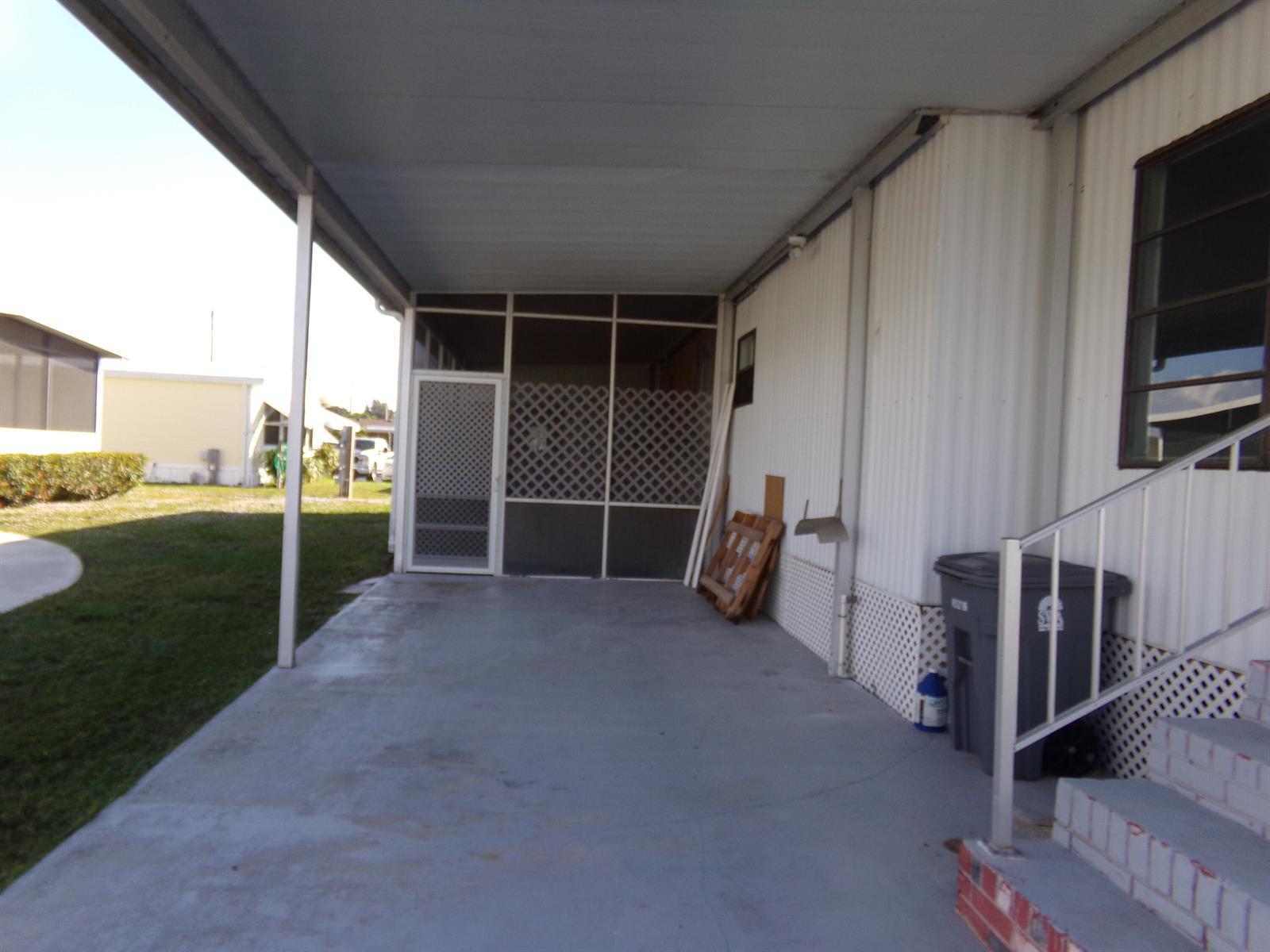 A covered concrete carport area features a screened-in porch entrance and white metal siding — 52004 Florinada Bay, Boynton Beach FL 33436, BOYNTON BEACH, FL