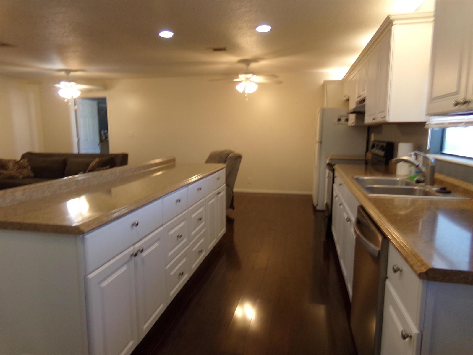 A kitchen with white cabinets, granite countertops, and dark hardwood floors opens to a living area — 52004 Florinada Bay, Boynton Beach FL 33436, BOYNTON BEACH, FL
