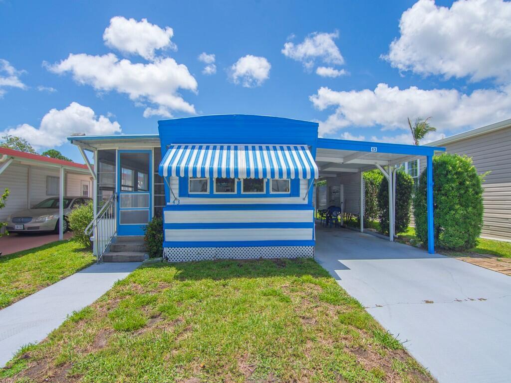 A blue and white mobile home features a striped awning, a carport, and a lawn — 4800 Federal Highway # 43, Stuart FL 34997, STUART, FL