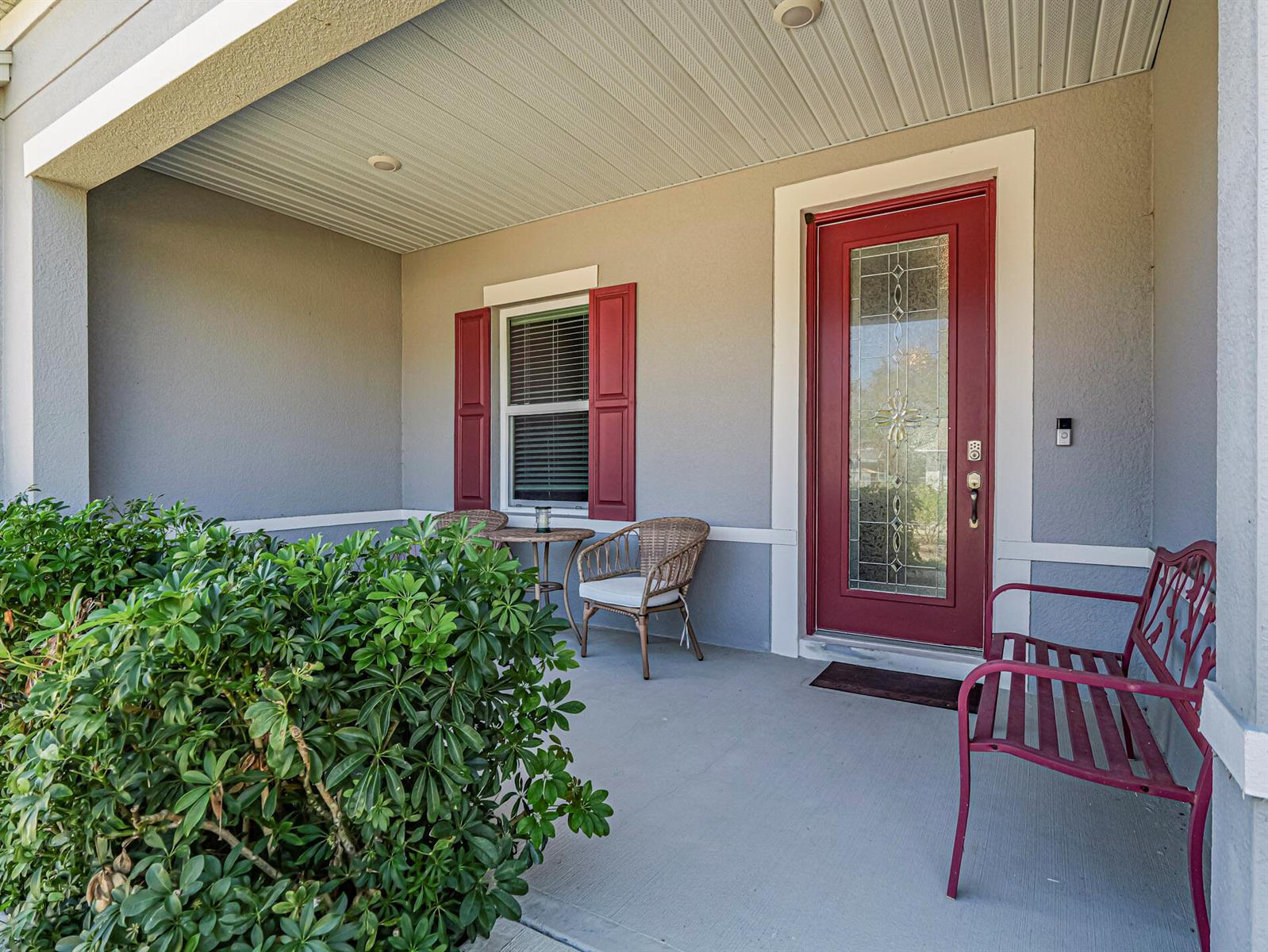 A covered front porch features a red door, a window with red shutters, and seating — 1031 Topsail Lane, Sebastian FL 32958, SEBASTIAN, FL