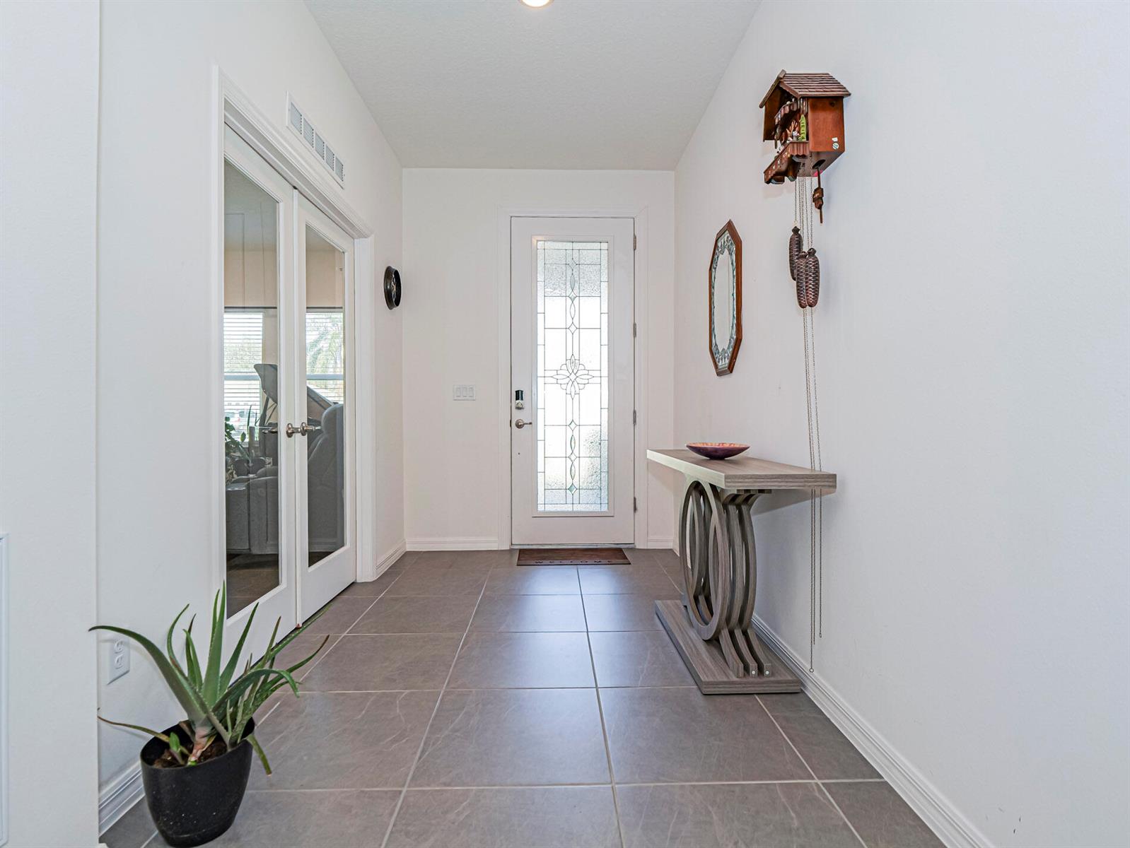 A bright entryway features gray tile flooring, a glass-paneled front door, and a console table — 1031 Topsail Lane, Sebastian FL 32958, SEBASTIAN, FL