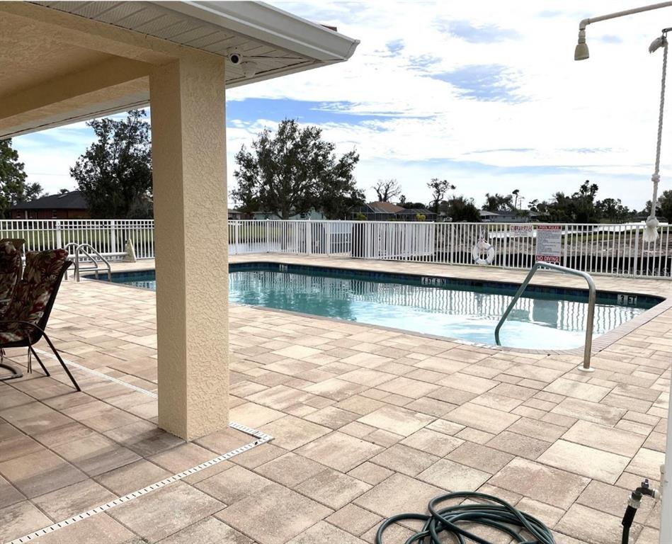 A paved patio overlooks a rectangular swimming pool enclosed by a white fence — 242 BOUNDARY BOULEVARD UNIT 111, ROTONDA WEST, FL