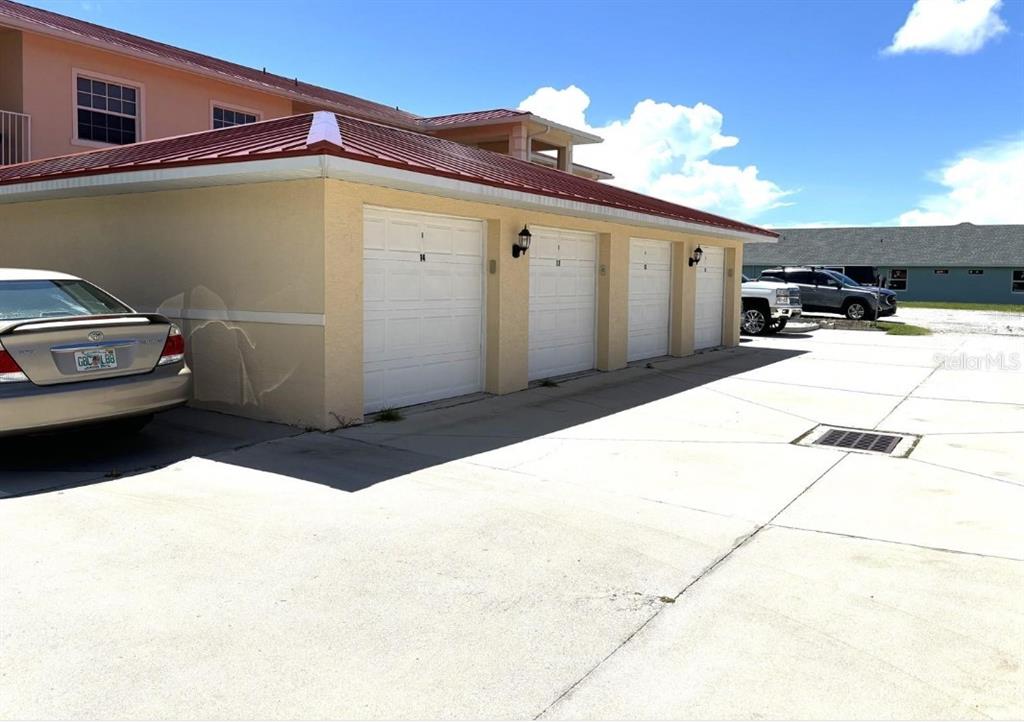 A row of four garage doors sits beneath a red metal roof on a building — 242 BOUNDARY BOULEVARD UNIT 111, ROTONDA WEST, FL