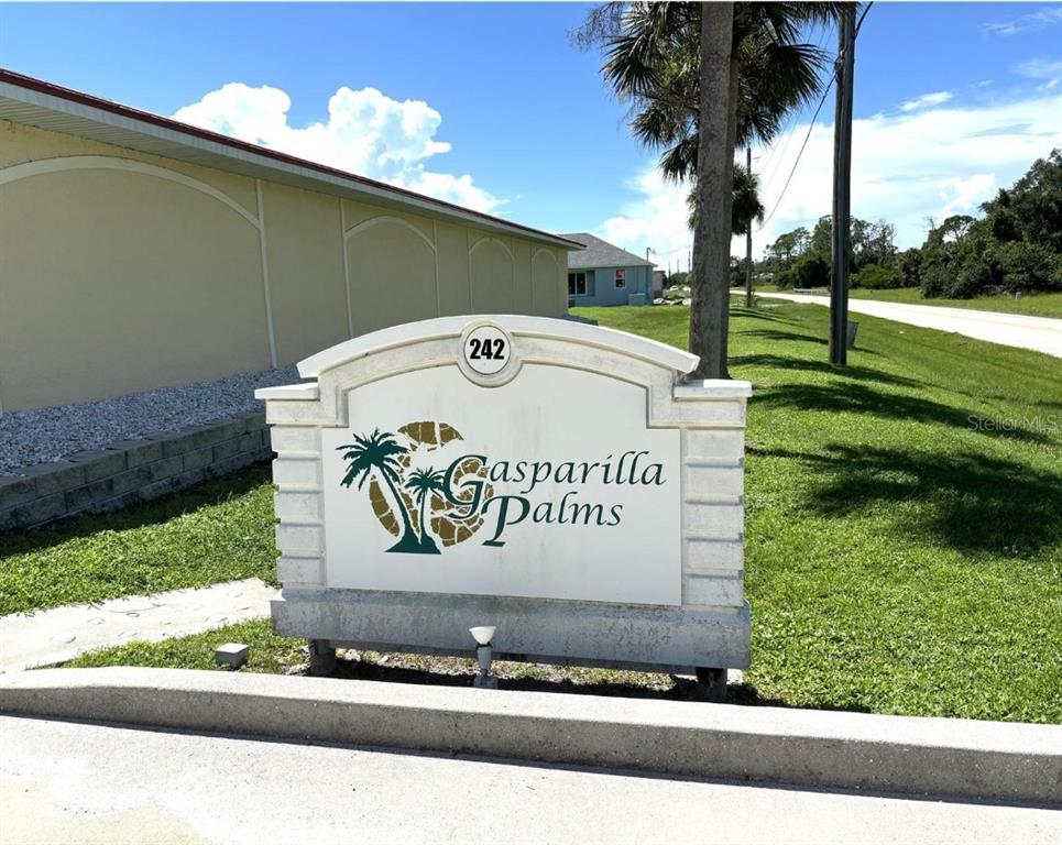 A white monument sign for Gasparilla Palms stands on a grassy lawn near a building — 242 BOUNDARY BOULEVARD UNIT 111, ROTONDA WEST, FL