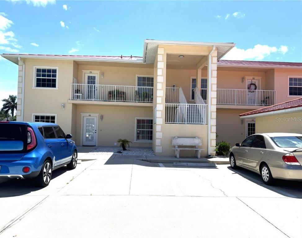 A two-story apartment building exterior with a concrete parking area and two parked cars — 242 BOUNDARY BOULEVARD UNIT 111, ROTONDA WEST, FL