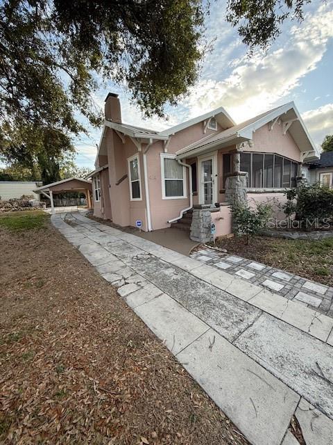 A pink cottage-style house features a stone chimney, a front porch, and a concrete driveway — 414 AVENUE C AVENUE NE, WINTER HAVEN, FL
