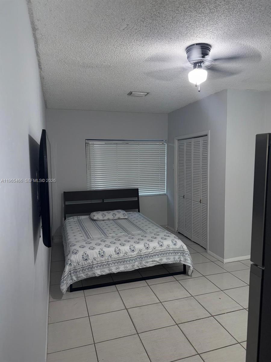 A bedroom features a bed, white-tiled floors, a ceiling fan, and a closet with louvred doors — 13142 SW 5th St # 0, Miami FL 33184, MIAMI, FL