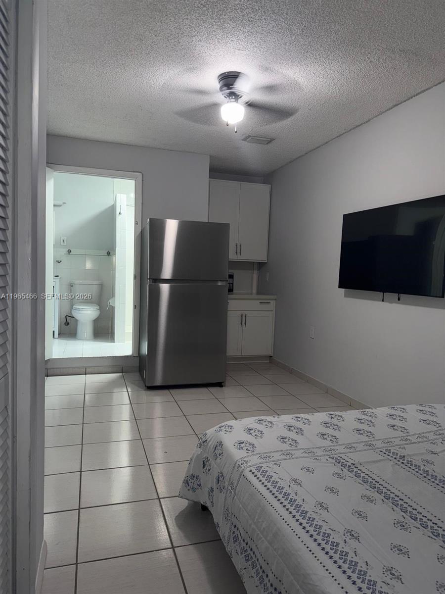A bedroom with a tiled floor, a stainless steel refrigerator, and an attached bathroom — 13142 SW 5th St # 0, Miami FL 33184, MIAMI, FL