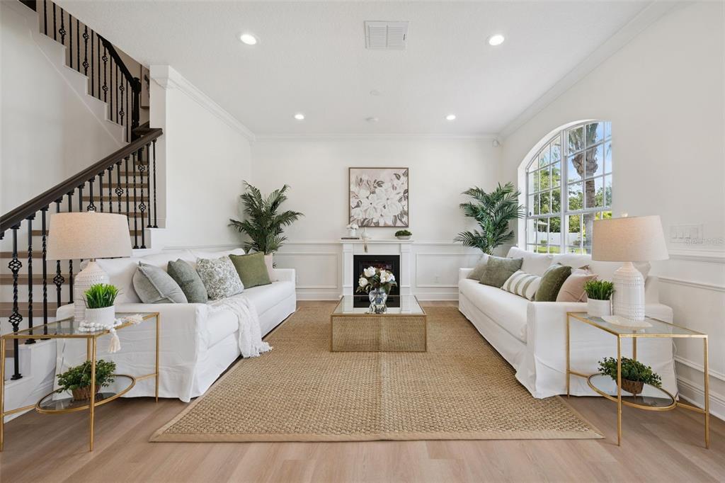 A bright living room features two white sofas, a central fireplace, and a wooden staircase — 5979 WINCHESTER ISLE RD, ORLANDO, FL
