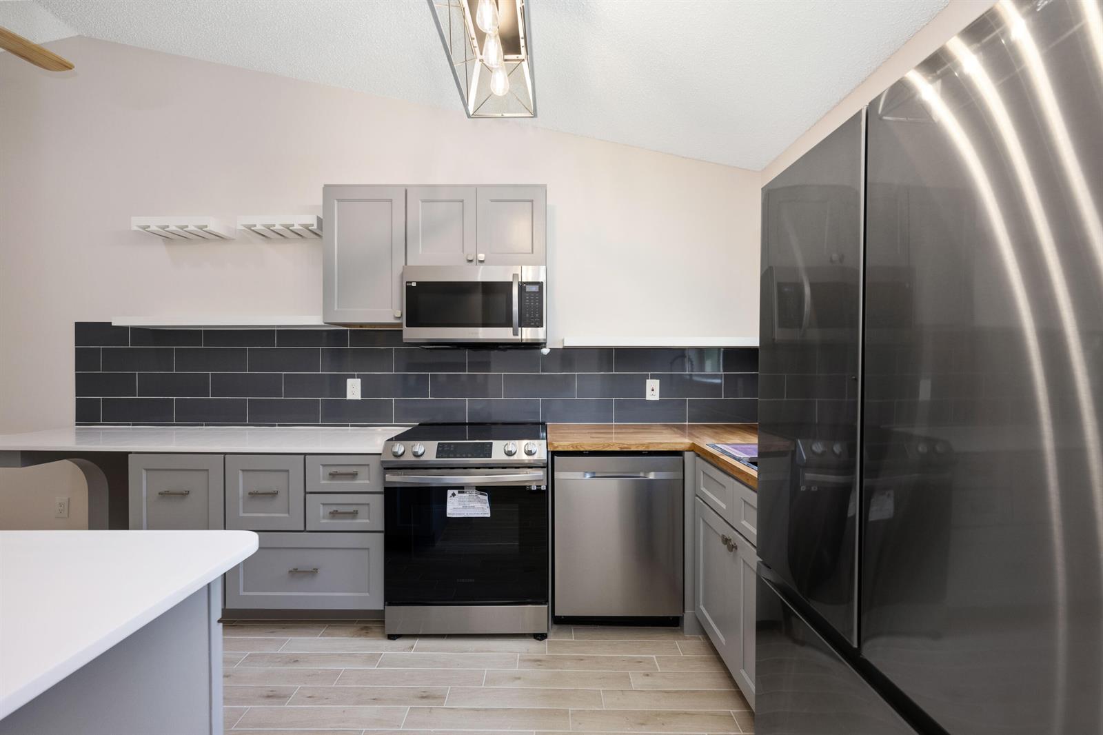 A kitchen features gray cabinets, stainless steel appliances, a dark tile backsplash, and wood countertops — 5214 Stacy Street # 3, FL 33417, FL