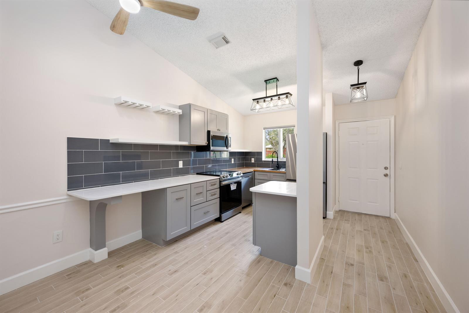 A kitchen features gray cabinets, white countertops, a dark tile backsplash, and wood-look tile flooring — 5214 Stacy Street # 3, FL 33417, FL