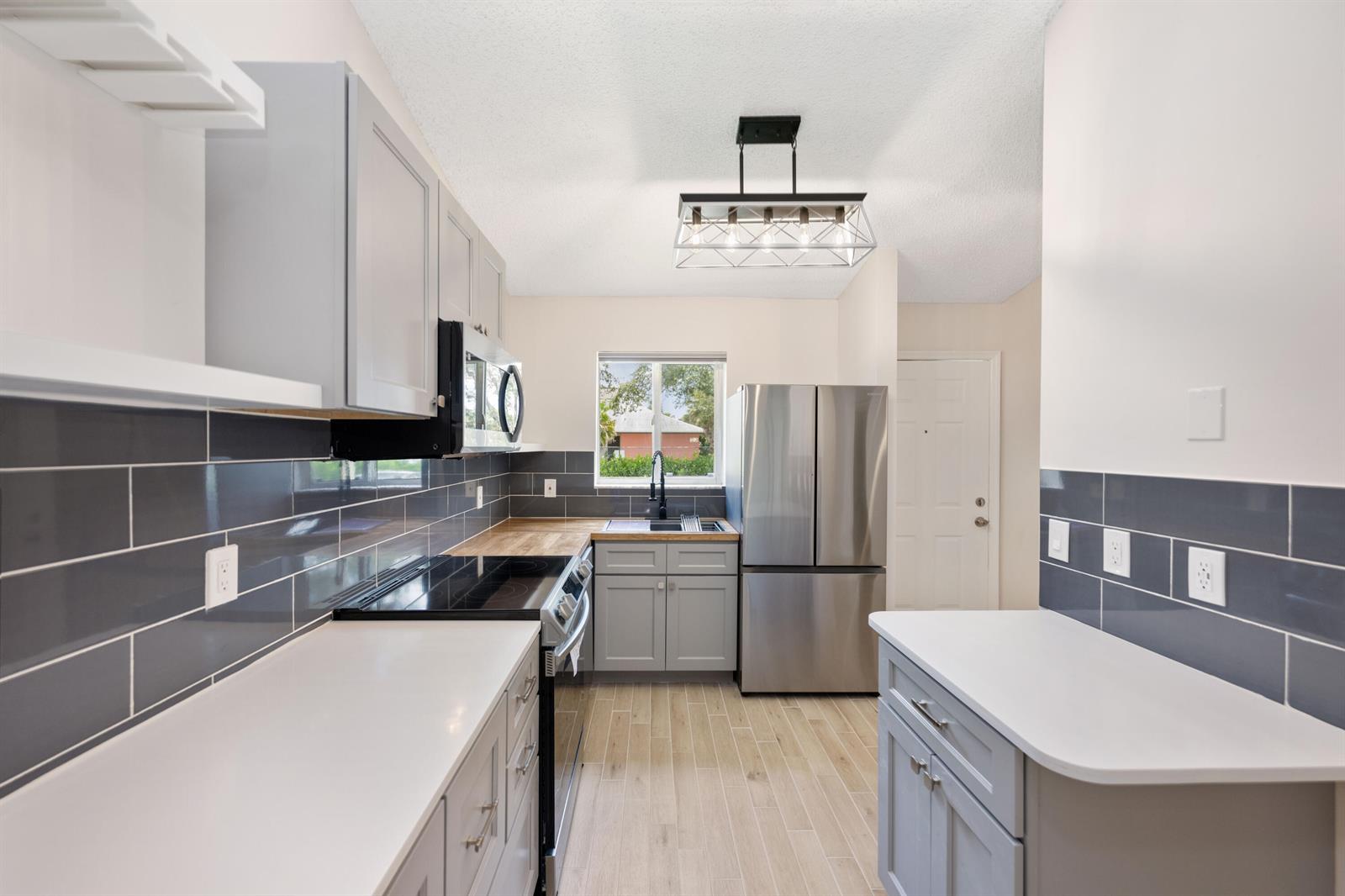 A kitchen features gray cabinets, stainless steel appliances, white countertops, and a dark tile backsplash — 5214 Stacy Street # 3, FL 33417, FL