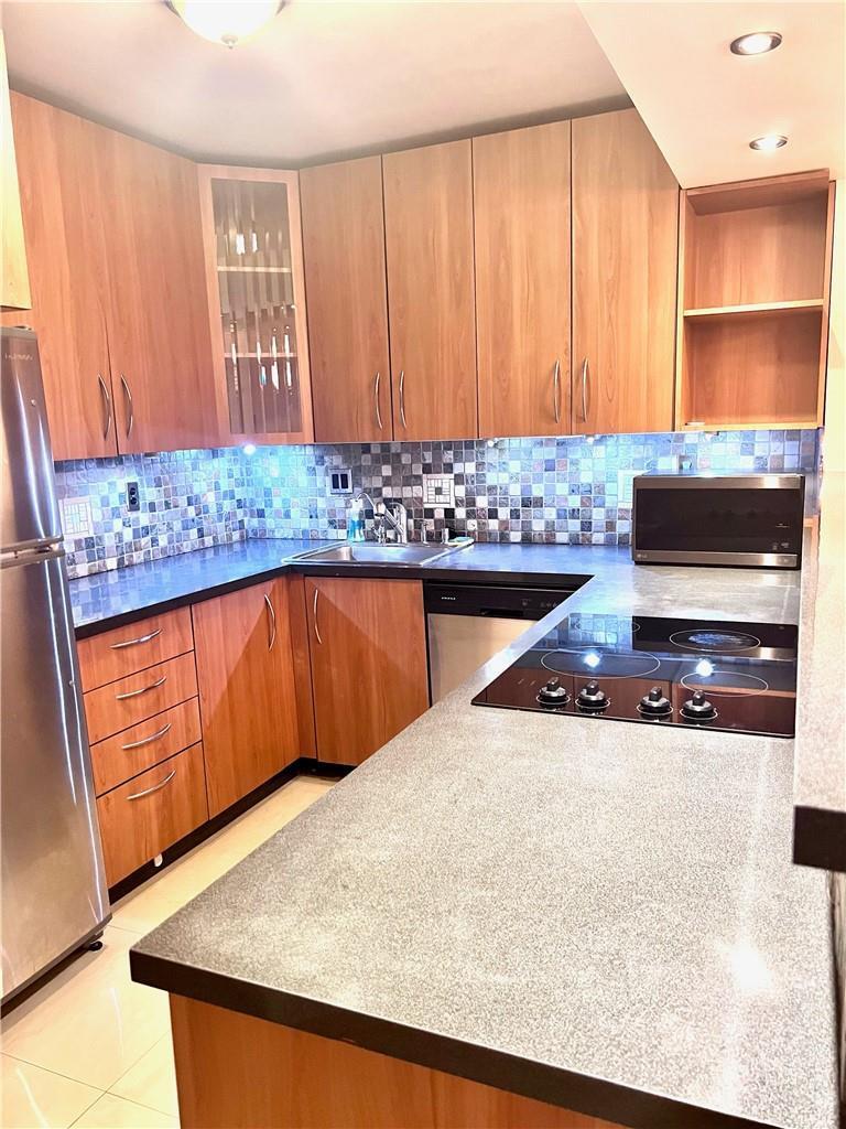 A kitchen with wood cabinets, a mosaic tile backsplash, and dark countertops — 600 Three Islands Boulevard # 1108, Hallandale Beach FL 33009, HALLANDALE BEACH, FL