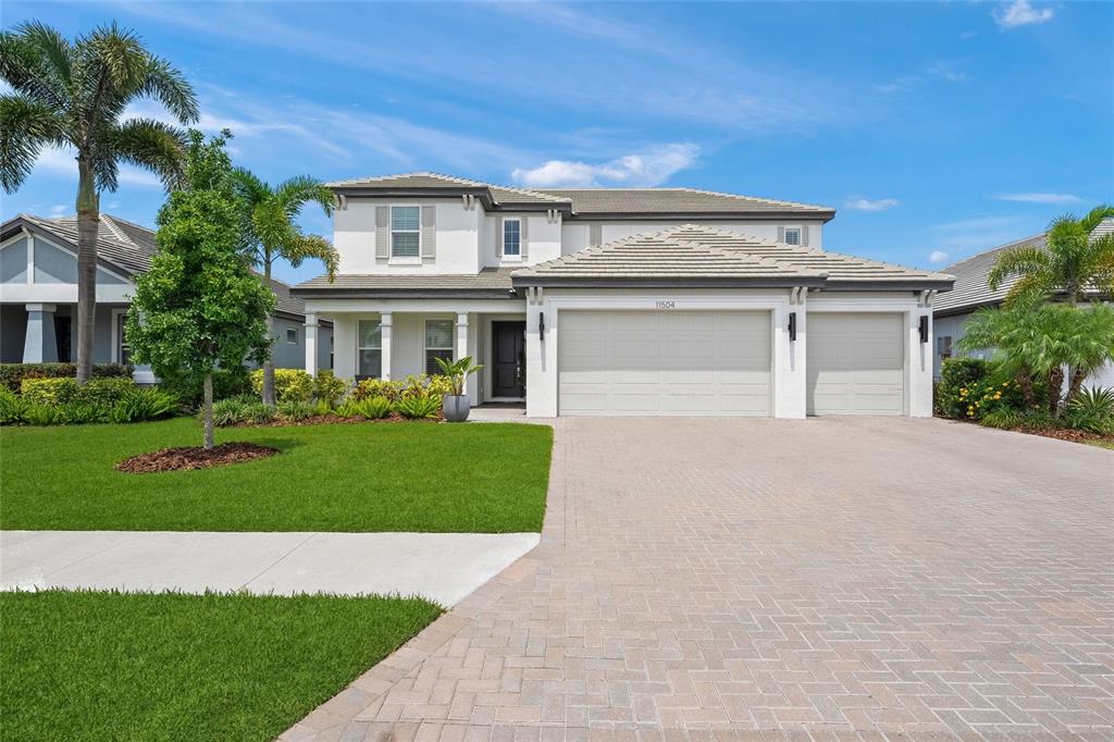 A two-story house with a paved driveway, a three-car garage, and a landscaped front lawn — 11504 APPLE TREE CIRCLE, BRADENTON, FL