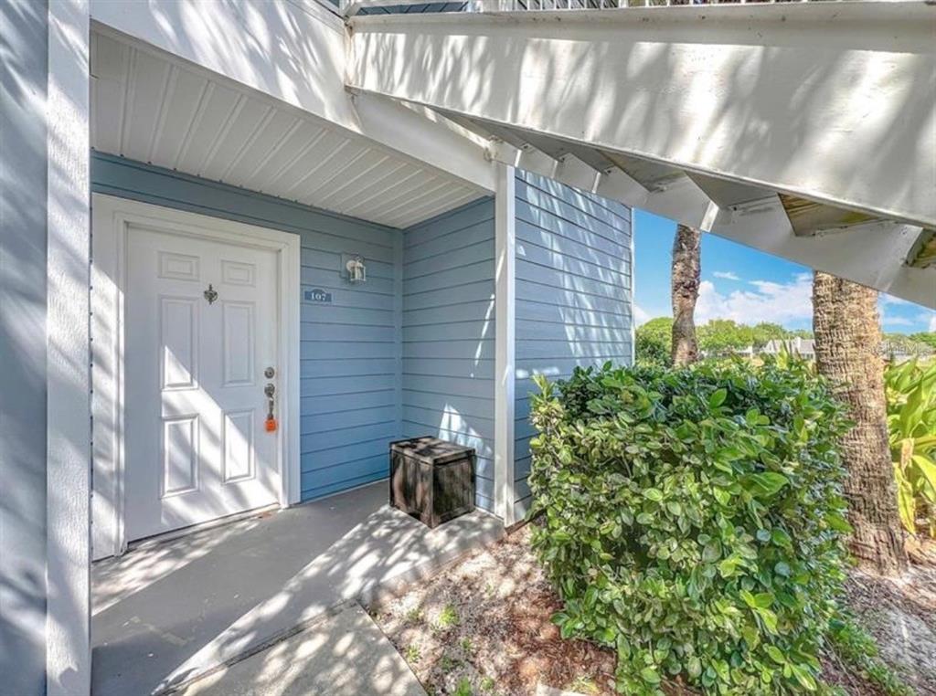 A white front door with the number 107 sits under a staircase next to a bush — 2513 GRASSY POINT DRIVE UNIT 107, LAKE MARY, FL