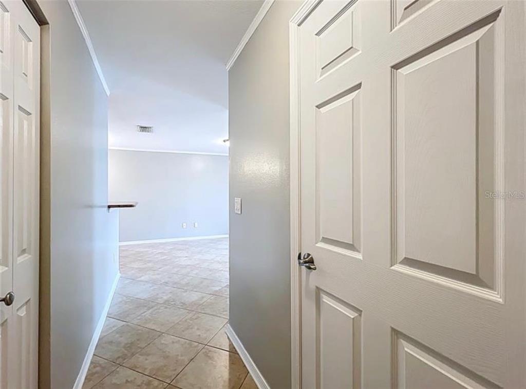 A hallway with tiled floors leads to an open living area between two white doors — 2513 GRASSY POINT DRIVE UNIT 107, LAKE MARY, FL