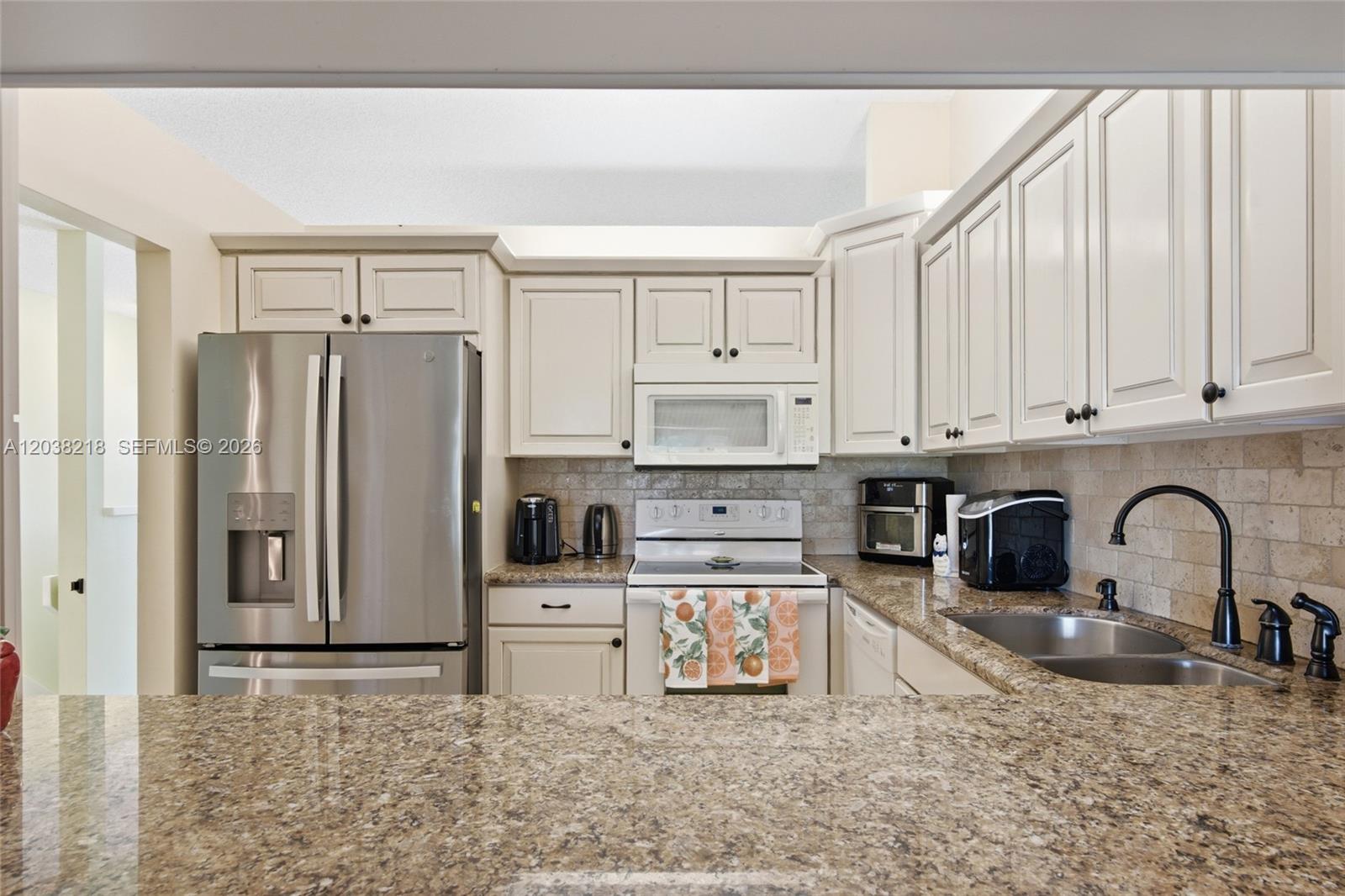 A kitchen features off-white cabinets, stainless steel appliances, and granite countertops with a tile backsplash — 104 Freedom Ct # 104, Deerfield Beach FL 33442, DEERFIELD BEACH, FL