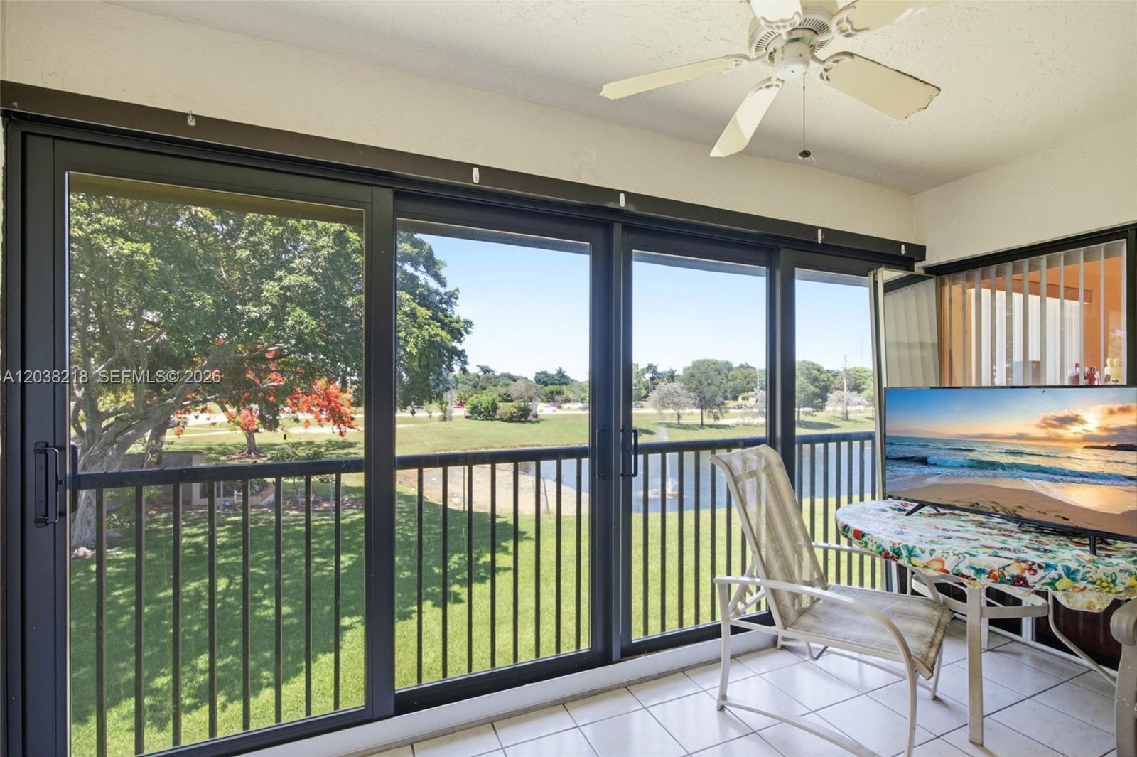 A tiled balcony features a ceiling fan, sliding glass doors, and a view of greenery — 104 Freedom Ct # 104, Deerfield Beach FL 33442, DEERFIELD BEACH, FL