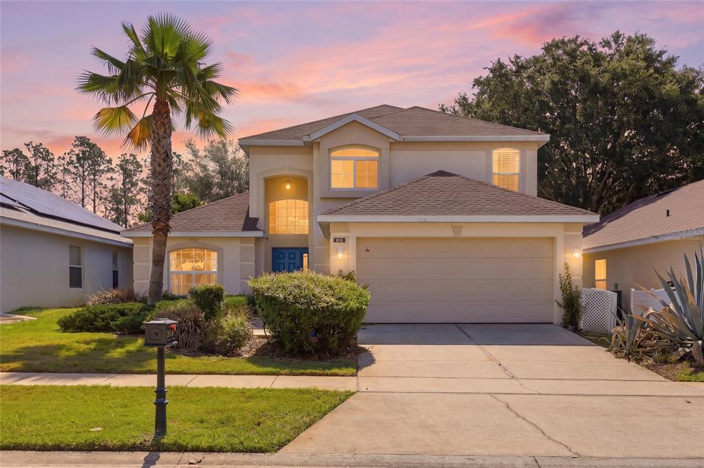 A two-story suburban house with a beige stucco exterior, a two-car garage, and a palm tree — 816 TROON CIRCLE, DAVENPORT, FL