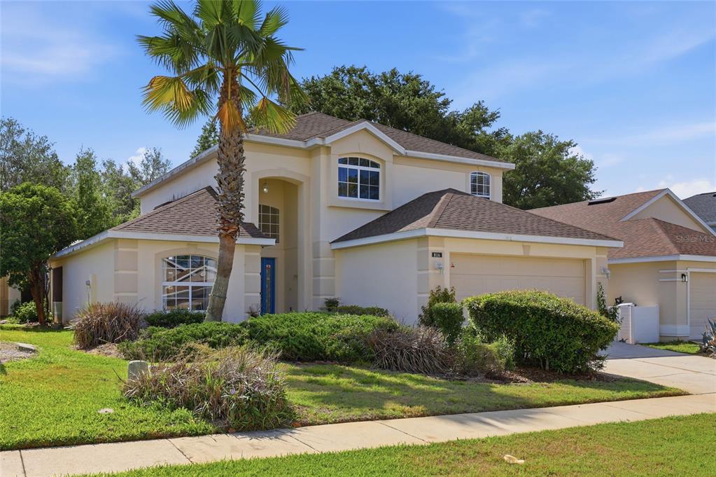 A two-story suburban house with a tan stucco exterior, a palm tree, and a garage — 816 TROON CIRCLE, DAVENPORT, FL