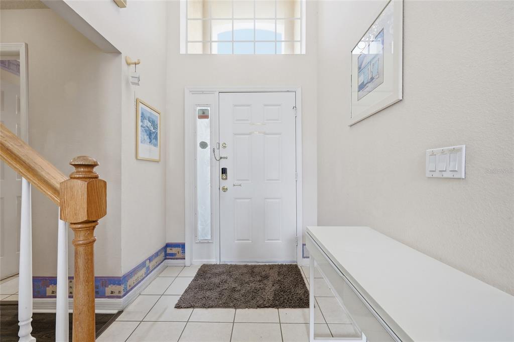 A bright entryway features a white front door, tiled floors, and a wooden staircase railing — 816 TROON CIRCLE, DAVENPORT, FL