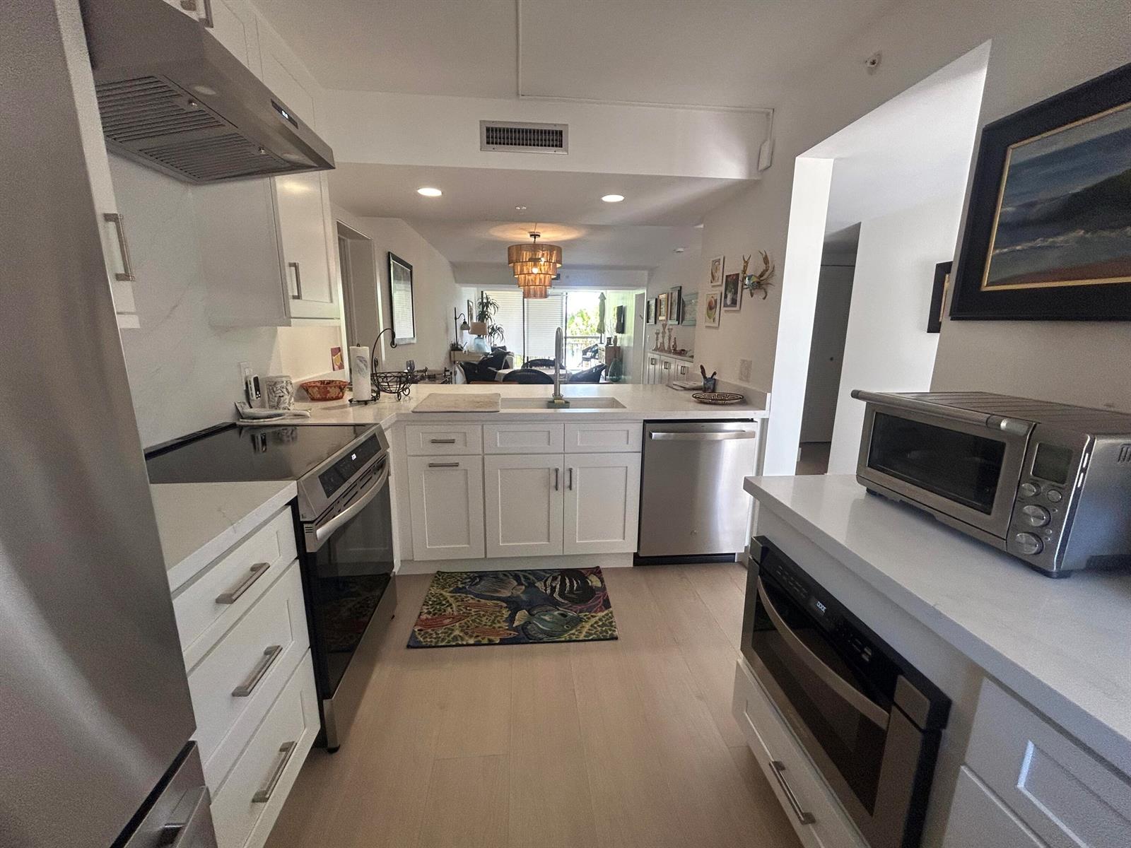 A modern white kitchen features stainless steel appliances, quartz countertops, and light wood flooring — 1901 Marina Isle Way # 302, Jupiter FL 33477, JUPITER, FL