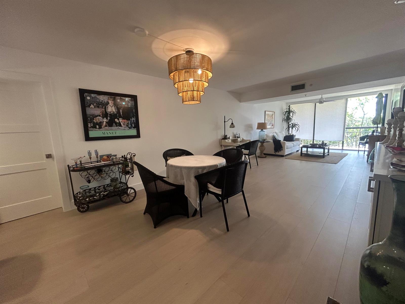 An open-concept living and dining area features light wood flooring and a tiered rattan chandelier — 1901 Marina Isle Way # 302, Jupiter FL 33477, JUPITER, FL