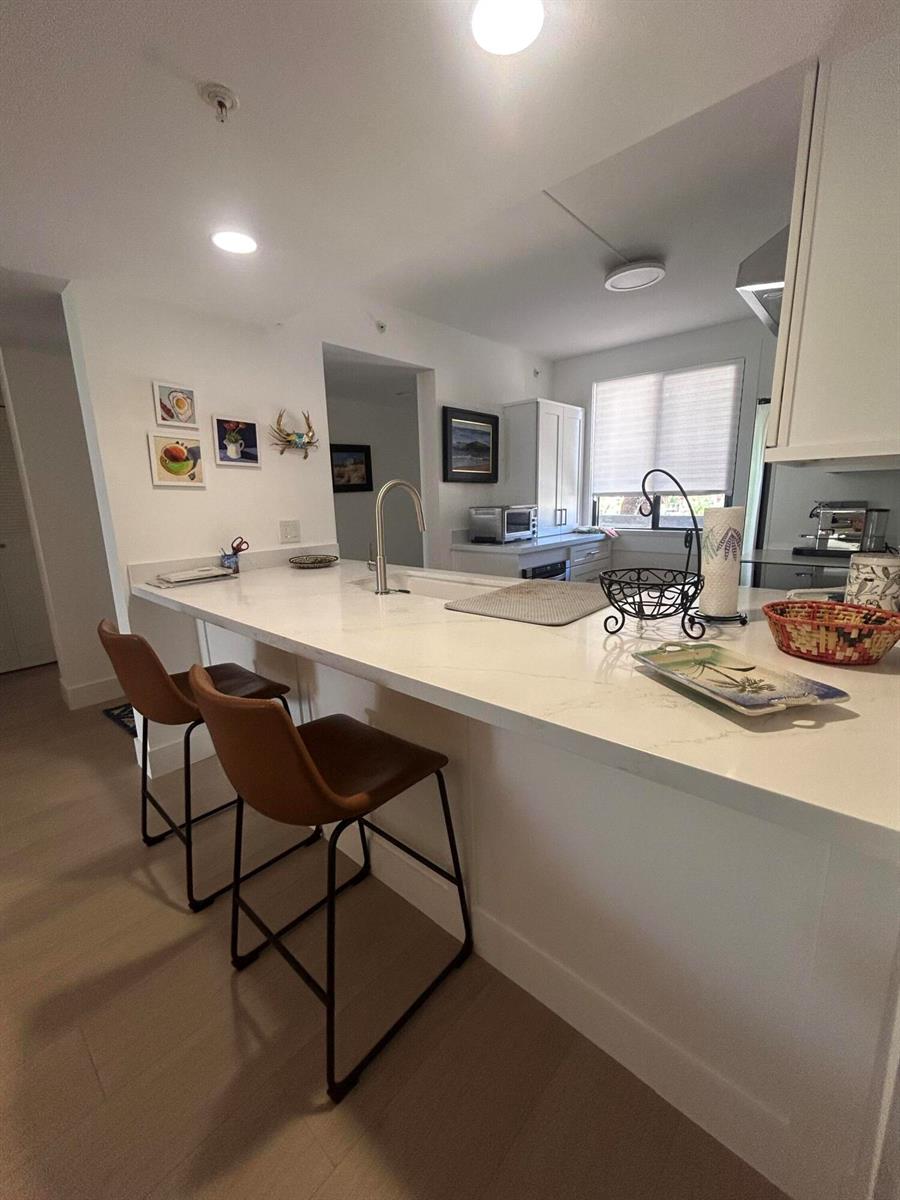 A kitchen features a white quartz island with two brown bar stools and light flooring — 1901 Marina Isle Way # 302, Jupiter FL 33477, JUPITER, FL