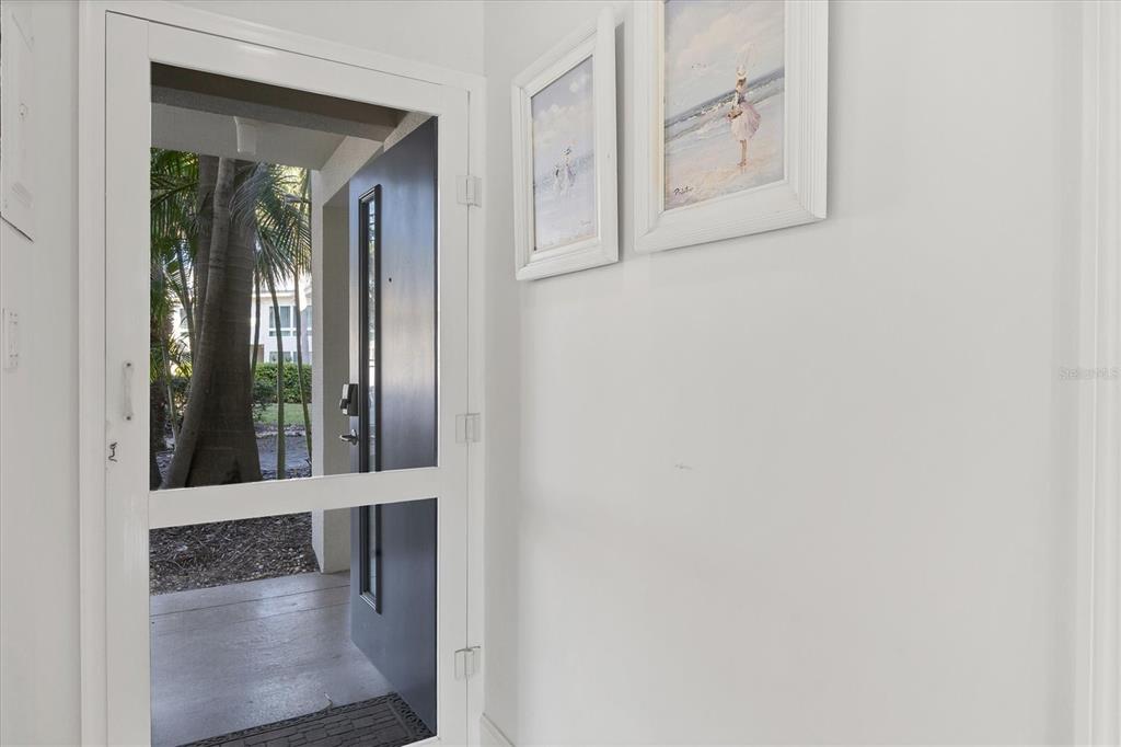 An open front door reveals a view of palm trees through a white screen door — 500 S WASHINGTON DRIVE UNIT 3A, SARASOTA, FL
