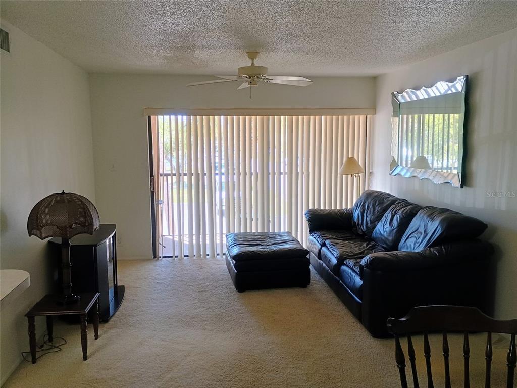 A living room features beige carpet, a black leather sofa, and a sliding glass door — 19505 QUESADA AVENUE UNIT CC205, PORT CHARLOTTE, FL