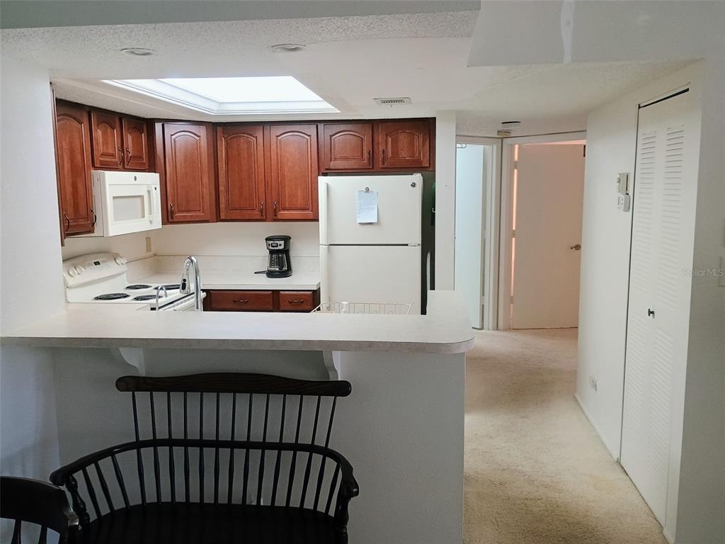 A kitchen with wood cabinets, white appliances, and a breakfast bar overlooks a carpeted hallway — 19505 QUESADA AVENUE UNIT CC205, PORT CHARLOTTE, FL