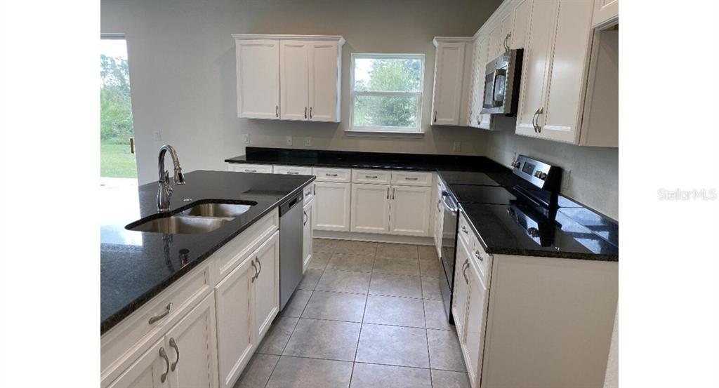 A kitchen features white cabinets, black countertops, stainless steel appliances, and light tile flooring — 5637 ABELMAN ROAD, NORTH PORT, FL