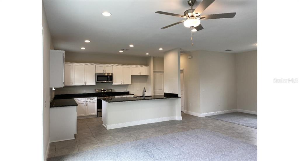 An open-concept kitchen features white cabinetry, black countertops, and tile flooring — 5637 ABELMAN ROAD, NORTH PORT, FL