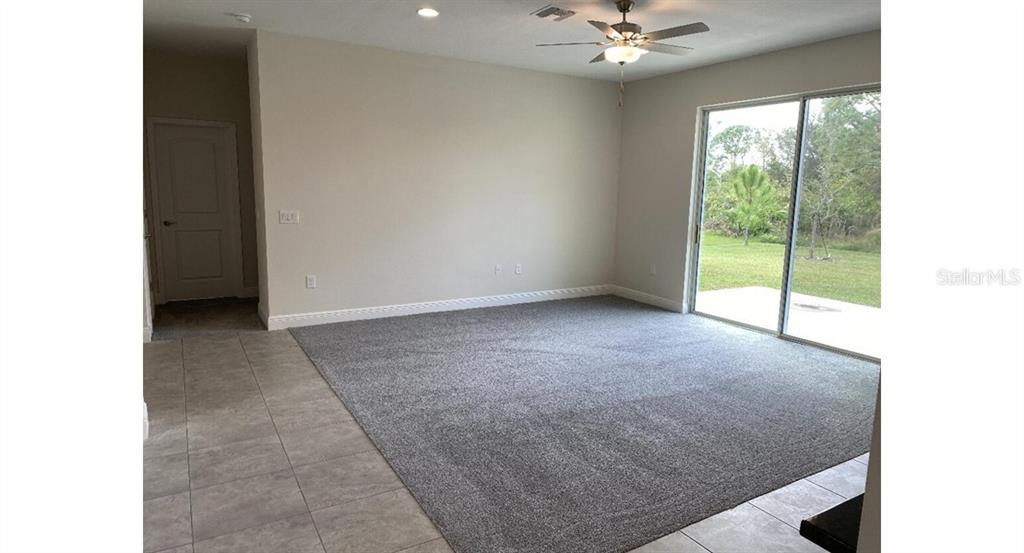 A living room with gray carpet, neutral walls, a ceiling fan, and sliding glass doors — 5637 ABELMAN ROAD, NORTH PORT, FL