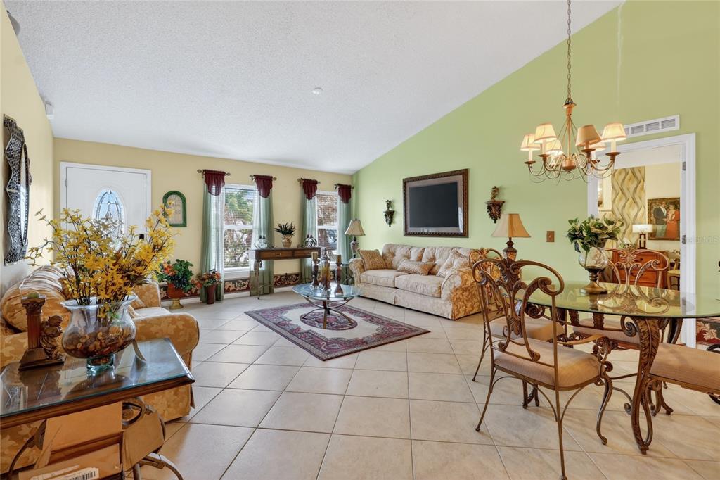 A living and dining area with tile floors, vaulted ceilings, and a green accent wall — 1912 LAKEVIEW PLACE, KISSIMMEE, FL