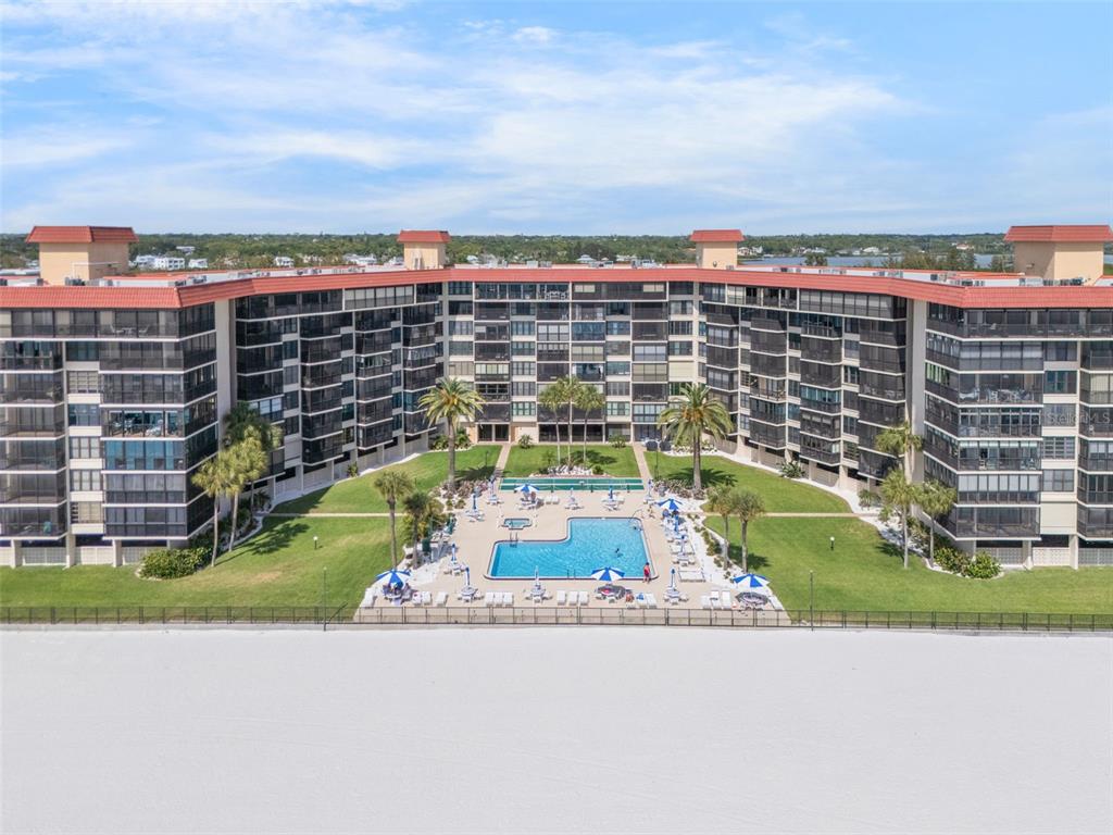 An aerial view shows a large beachfront apartment complex with a central swimming pool area — 18304 GULF BOULEVARD UNIT 105, REDINGTON SHORES, FL
